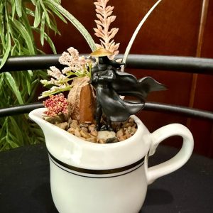 Wandering-Ronin-Pitcher-Garden Ronin figurine in a white pitcher with flowing cape and decorative plants and stones.
