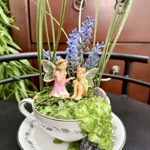 fairy-waterfall-teacup-garden-lavender-crystal-decor A teacup featuring two fairies seated among faux lavender and grass with a cascading green crystal waterfall spilling over the side.