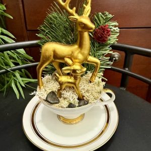 gold-deer-family-holiday-centerpiece-teacup Golden reindeer figurines, including a stag and fawn, arranged on moss in a teacup with evergreen and pinecone accents.