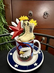 A patriotic mug with a bald eagle design is filled with miniature army boots, yellow flowers, and a red star, creating a tribute to military service.