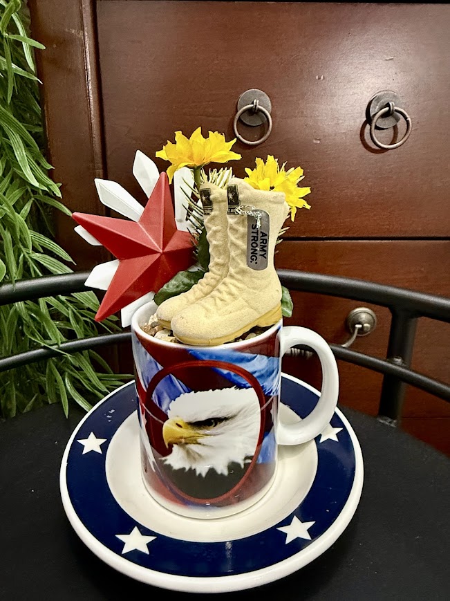 A patriotic mug with a bald eagle design is filled with miniature army boots, yellow flowers, and a red star, creating a tribute to military service.