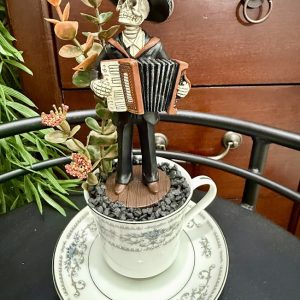 skeleton-mariachi-accordion-day-of-dead-cup Day of the Dead skeleton in a sombrero playing an accordion, arranged with artificial foliage in a white and silver teacup and saucer.